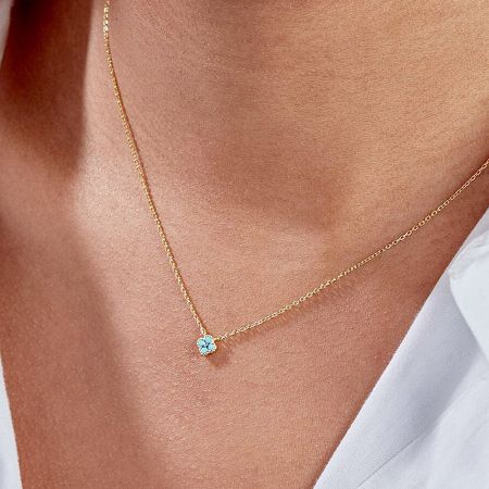 Close-up of the gold necklace with a turquoise petal pendant worn on the neck.