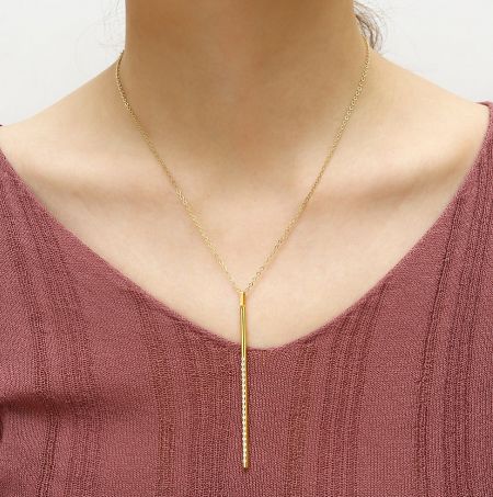 Detailed view of the gold necklace featuring a long, thin bar pendant.