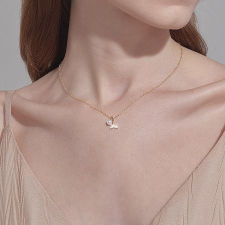 Close-up of a gold necklace featuring a wing-shaped charm and a pearl.