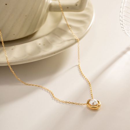 Close-up detail of the irregular pearl pendant on the gold stainless steel necklace.