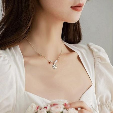 Set di collane choker a forma di rosa vuota placcate in oro con perle - Una modella con lunghi capelli castani che indossa l'elegante collana choker placcata in oro a forma di rosa, mostrando la sua lunghezza e il design delicato del pendente su una camicia bianca.