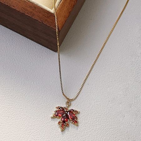 Close-up view of the red zircon crystal maple leaf pendant on its gold chain.