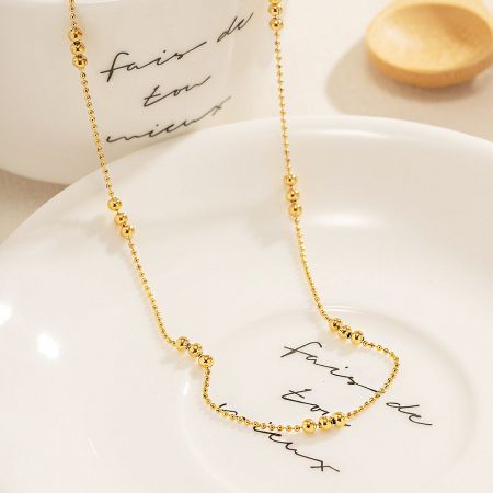 The gold beaded necklace elegantly displayed on a decorative white plate.