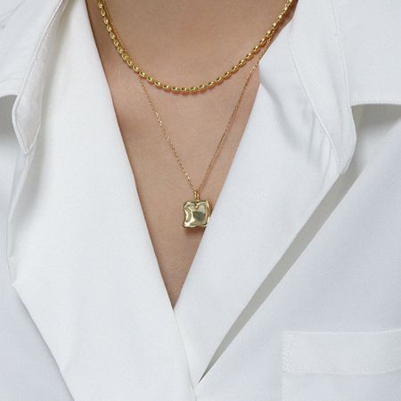 Model wearing the gold square charm necklace layered with another chain, demonstrating its versatile styling.