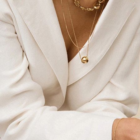 The gold ball necklace layered with other chains against a crisp white blazer.