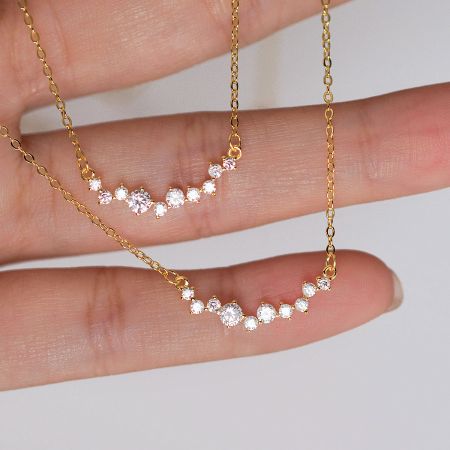 Close-up of two gold-plated 925 silver smile necklaces with CZ stones, held in hand to show detail.