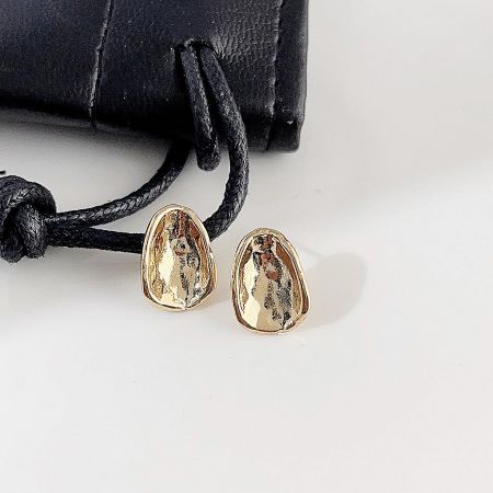 Detailed product shot of the gold-plated oval stud earrings with a black pouch in the background.