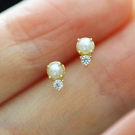 Close-up of a gold stud earring with a central pearl surrounded by small cubic zirconia stones.