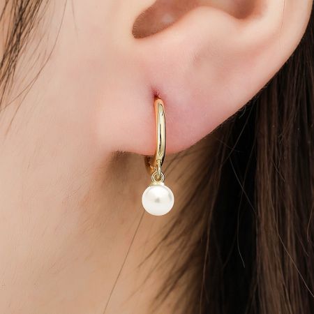 Close-up of the pearl huggie hoop earring being worn, showing its luster.