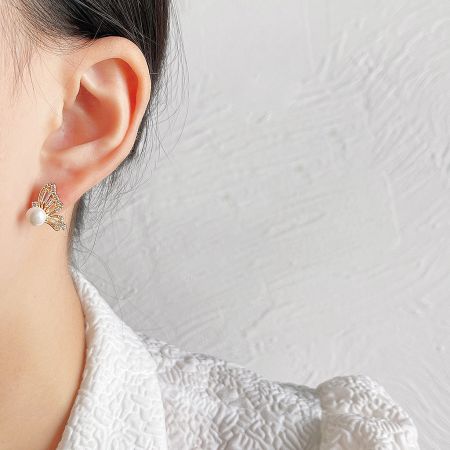Close-up view of the dainty butterfly zircon pearl earring on an ear.