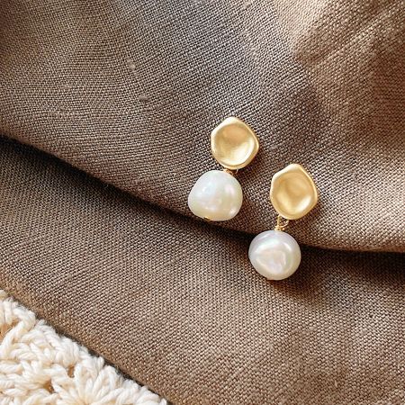 Another perspective of the gold and pearl earrings on a textured white surface.
