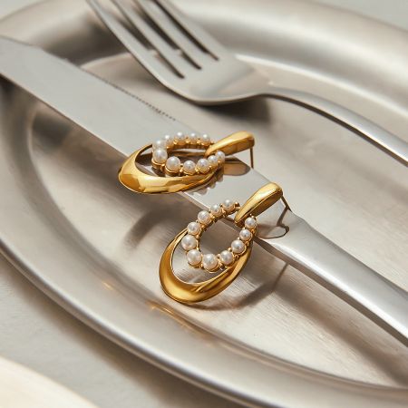Elegant arrangement of stainless steel pearl earrings with titanium studs on a silver plate with cutlery.