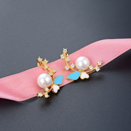 Close-up view of the pearl butterfly earring showcasing the intricate floral design with blue and white enamel petals and a central pearl.