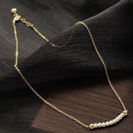 Close-up of the delicate chain and pearl clasp on the gold-plated necklace.