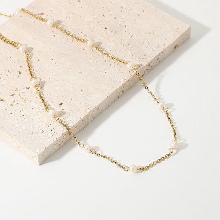 Detailed product shot of the pearl charm necklace on a decorative surface.