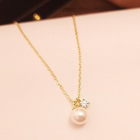 Clear view of the sparkling zircon stone next to the pearl on the gold necklace.