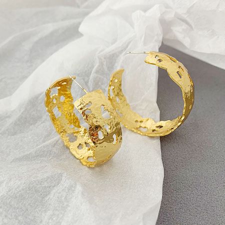 A pair of gold perforated hoop earrings with a unique, handmade aesthetic against a neutral background.