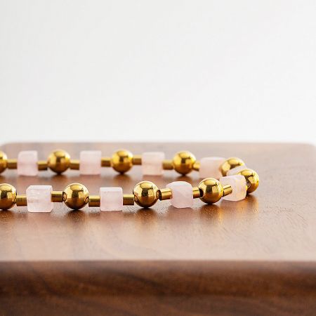 Macro shot highlighting the texture and detail of the gold beads and pink stone cubes.