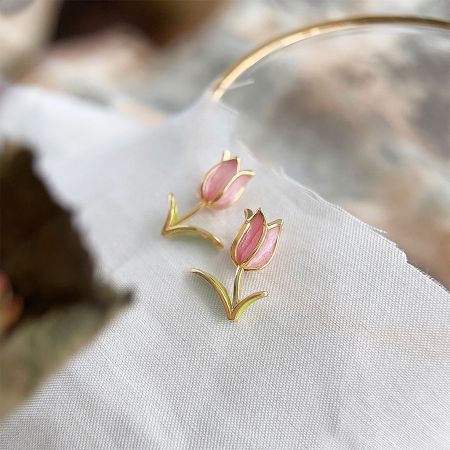 Close-up view of the gold and pink enamel tulip earrings on a neutral background.