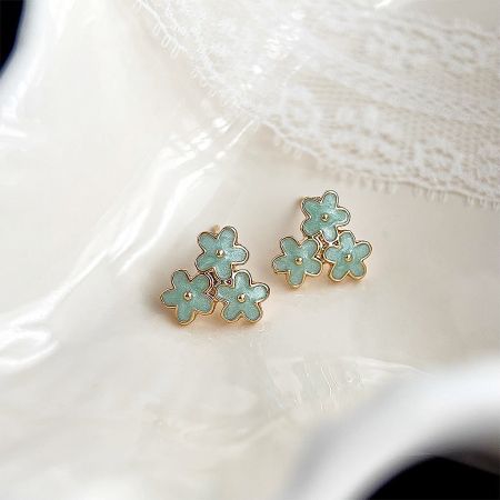 A pair of flower-shaped earrings with a gold-plated setting and light blue-green enamel details.