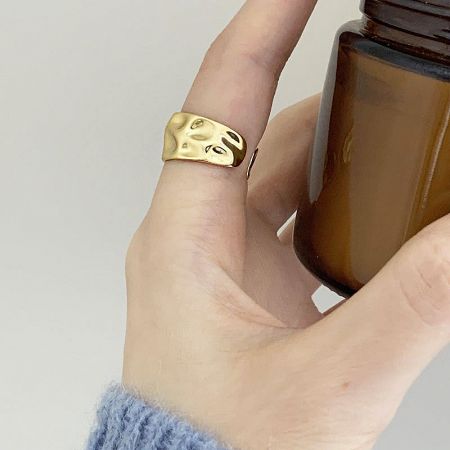A gold hammered geometric ring styled next to a decorative brown bottle.