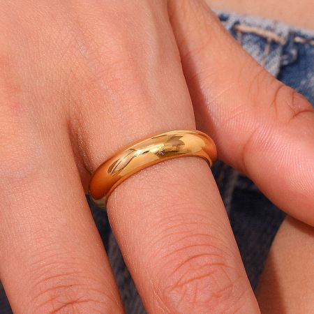 Close-up of the thick gold band ring worn on a finger, showcasing its polished finish.