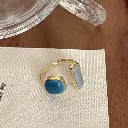 Detailed view of a gold-plated brass ring with blue and white enamel stones on a white surface.