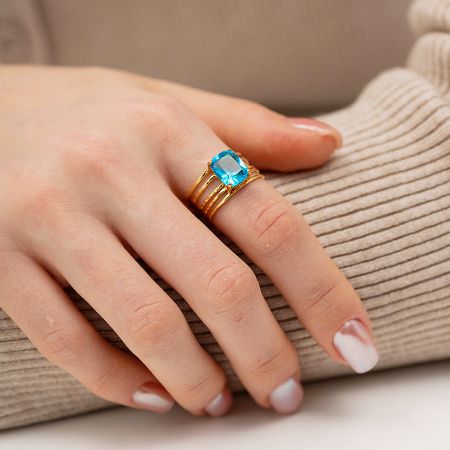 Blue Rectangle Zirconia Multilayer Stainless Steel Gold Open Finger Rings Set of 5 - A close-up of a woman's hand wearing the multilayer stainless steel ring with a gold finish, featuring a prominent rectangular blue zirconia gemstone. The ring has a unique stacked band design.