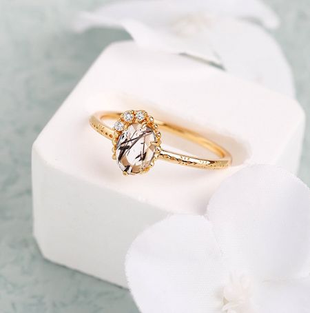 The gold-plated sterling silver ring with a prominent salt and pepper gemstone, presented elegantly in a white jewelry box.