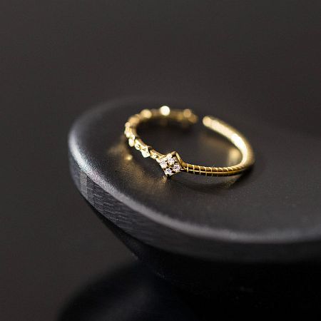 Studio product shot of the gold minimalist ring on a display stand, showing its intricate twist pattern.