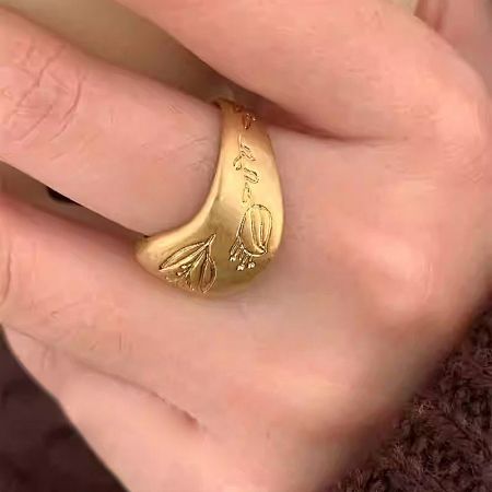 A hand holding the gold floral design brass ring to show scale.