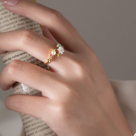 Gold ring with a central pearl and a white flower-shaped gemstone.