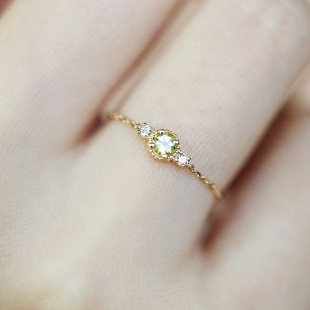 An elegant ring from the collection featuring a peridot-like green gemstone surrounded by smaller stones.