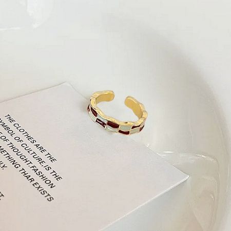 A stylish gold-plated enamel ring resting on a book, showcasing its detailed craftsmanship.