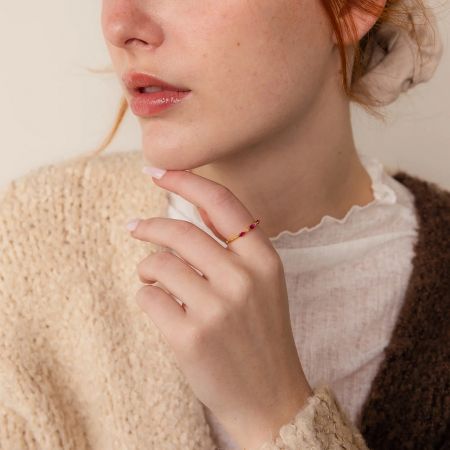 A woman's hand wearing a delicate gold-plated ring with red marquise and round gemstones.