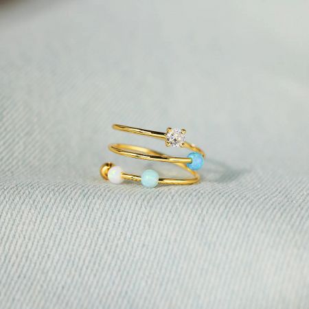 A product shot of the gold-plated Starlit Ocean ring, highlighting the triple-band design with opal and zircon stones.