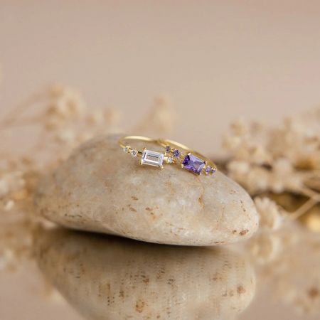 The sterling silver baguette CZ promise rings in white and purple, showcased on a decorative stone.