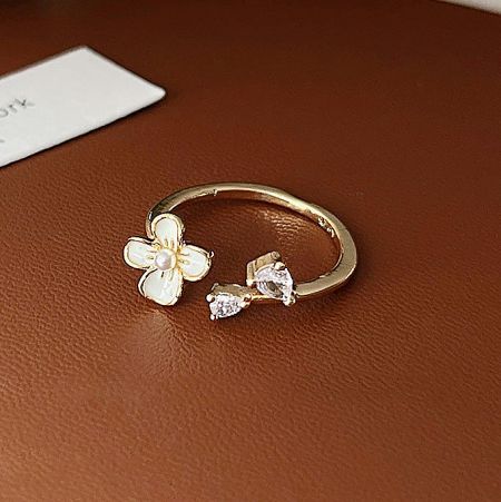 Elegant gold-plated ring featuring a white enamel flower and clear gemstones.