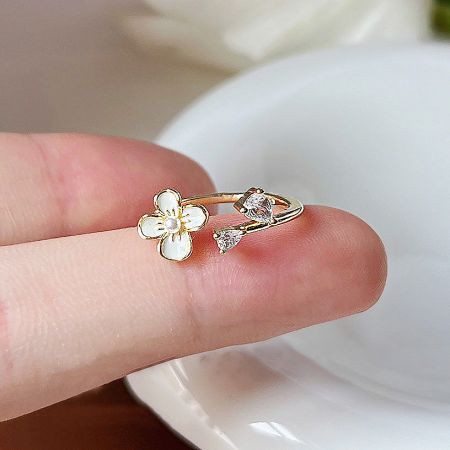 Close-up of a gold open-finger ring with a white flower and two brilliant zircon stones.