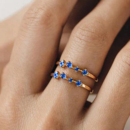 Two gold-finished stacking rings with blue zircons worn on a hand.