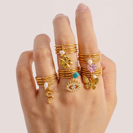 Model's hand wearing multiple gold-plated charm rings from the collection.