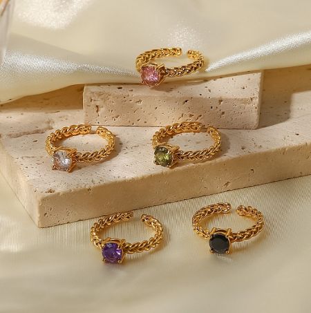 Close-up of five gold-plated stainless steel rings with colorful gemstone settings.