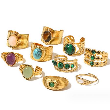 A variety of gold-plated stainless steel rings featuring different colored semi-precious gemstones, shown against a plain background.