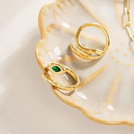 Two gold snake rings with gemstones elegantly displayed on a decorative white dish.