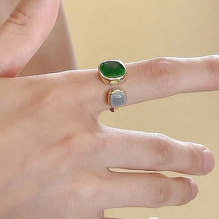 Two gold rings with green and white enamel stones worn on a hand to show scale.