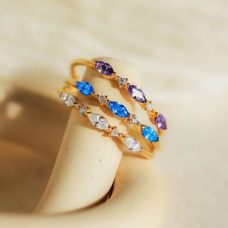 Three minimalist gemstone rings in purple, blue, and clear, displayed on a stand.