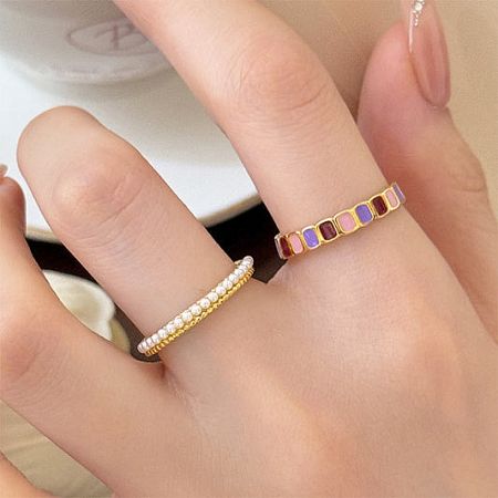 A hand modeling a set of stackable gold rings with colorful enamel and pearl details.