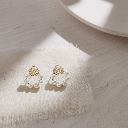 A pair of gold rose and pearl earrings displayed on a neutral background.