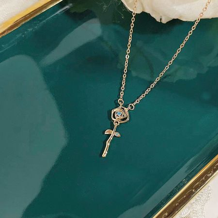 Close-up of the gold rose pendant necklace on a dark teal tray, highlighting the intricate details.