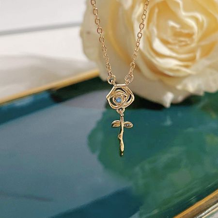 Detailed view of the gold rose pendant, showcasing the central blue gemstone.